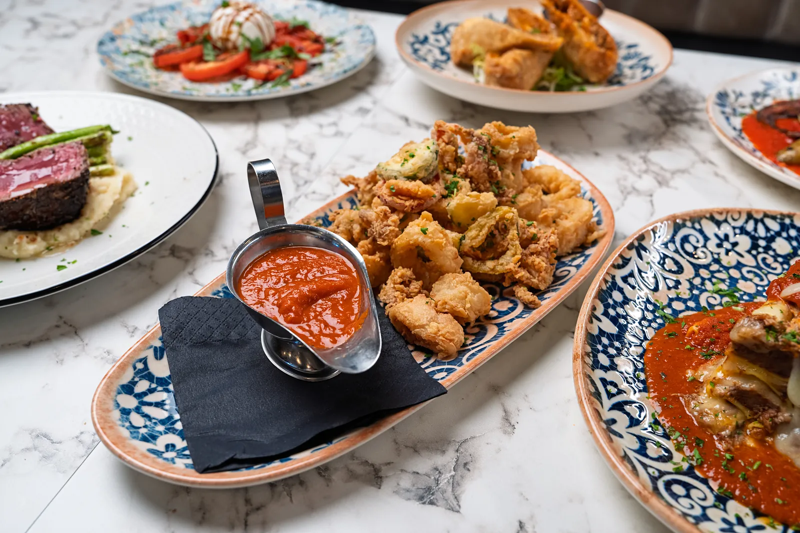Platter of crisp fried calamari and zucchini with a steel boat of marinara on a blue and white platter