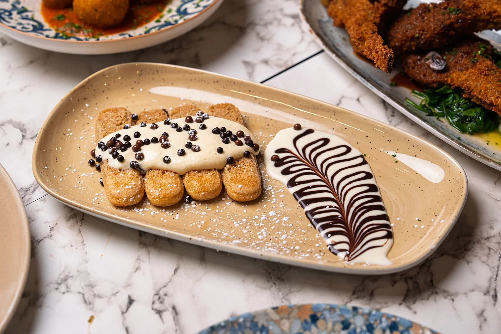 Dessert platter with sweet cream, chocolate pearls and a chocolate swirl beside crisp dippers on a tan plate