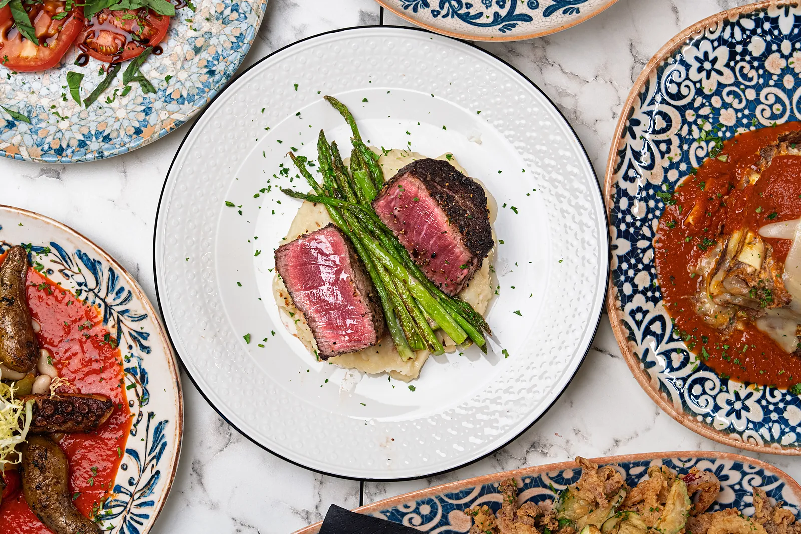 Overhead view of a seared filet and asparagus on mashed potato on a white plate with a navy rim