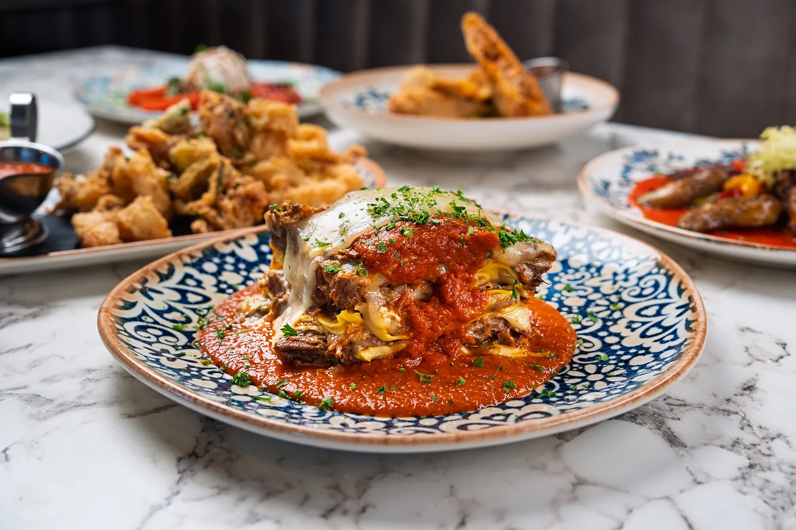 Baked parmigiana layered with melted mozzarella in tomato sauce on a blue and white majolica plate