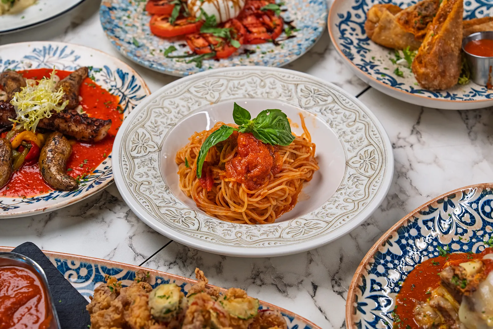 Spaghetti pomodoro with basil in an embossed white bowl on a marble table